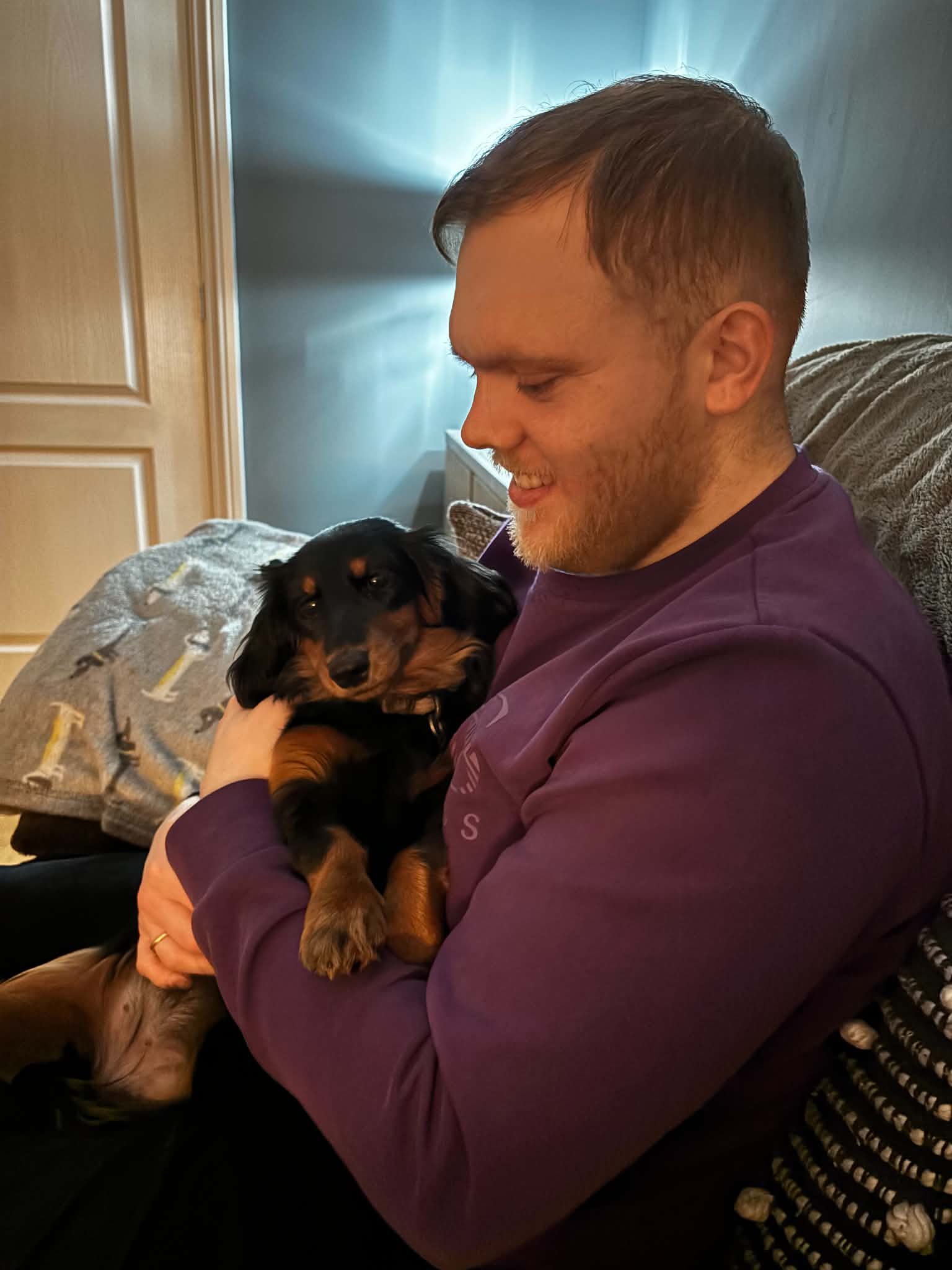 Dan cuddling a black and tan dachshund on the sofa