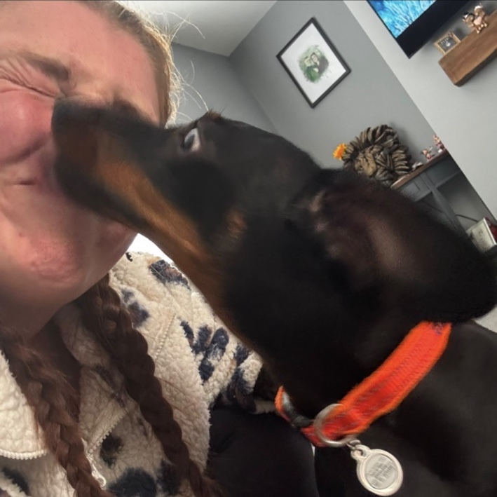 Katie laughing as a black and tan dachshund gives her a kiss